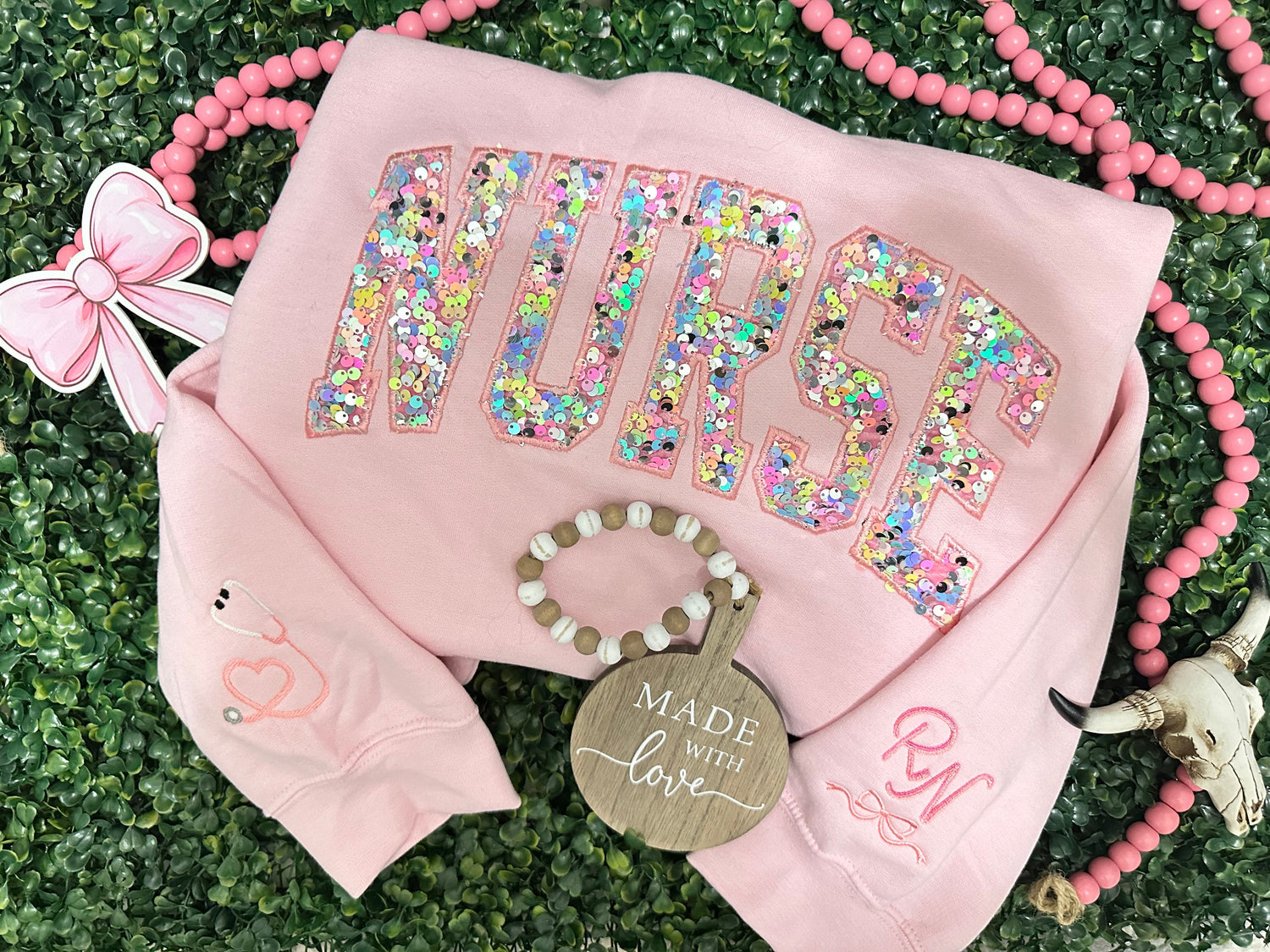 Pink 'NURSE' sweatshirt with glittery letters on a green grass background