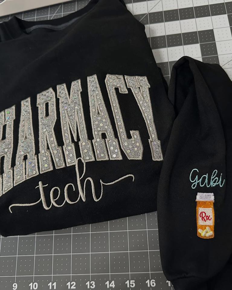 Black sweatshirt with 'pharmacist tech' text and a black hoodie with a small patch on a grid background.